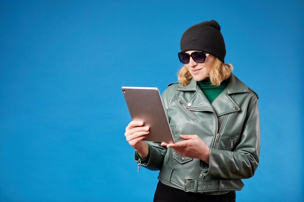 Vue latérale d'une jeune femme à l'aide d'une tablette isolée sur fond bleu Portrait en studio d'une jeune femme blonde séduisante à l'aide d'une tablette contre un mur bleu