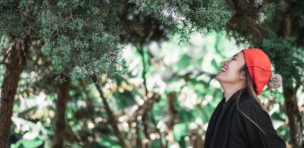 Vue latérale d'une jeune femme asiatique heureuse en costume d'hiver relaxante en respirant de l'air frais à l'extérieur dans la forêt avec espace de copie Concept de vacances et de voyage