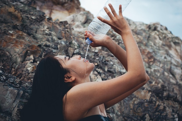 Photo vue latérale d'une jeune femme buvant de l'eau d'une bouteille