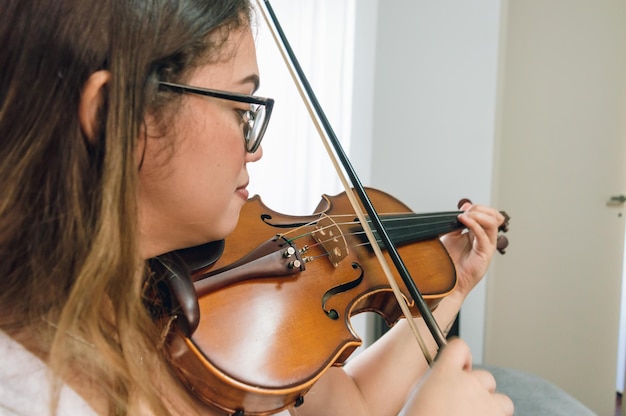 Vue latérale jeune femme caucasienne latine jouant du violon à la maison se bouchent