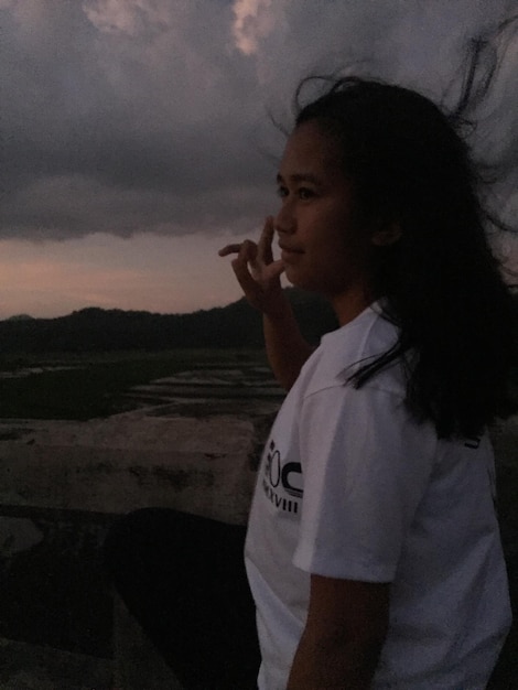 Photo vue latérale d'une jeune femme debout contre un ciel nuageux au coucher du soleil