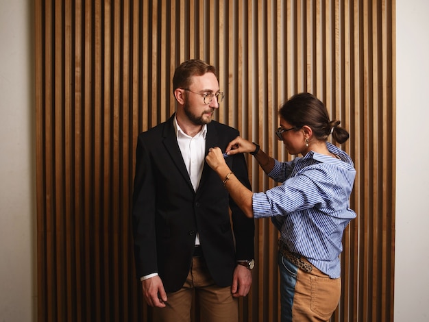 Vue latérale d'une jeune femme élégante ajustant la veste d'un homme mignon dans un intérieur d'appartement moderne.