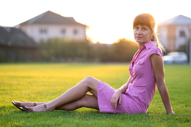 Vue latérale de la jeune femme mignonne assise sur l'herbe par beau temps