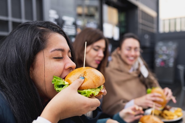 Vue latérale jeune femme mordant un hamburger. Les femmes assises à table au restaurant.