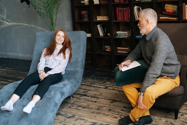 Vue latérale d'une jeune femme rousse déprimée parlant de problèmes allongés dans un fauteuil confortable dans une salle de déchargement psychologique. . Concept de traitement psychologique.