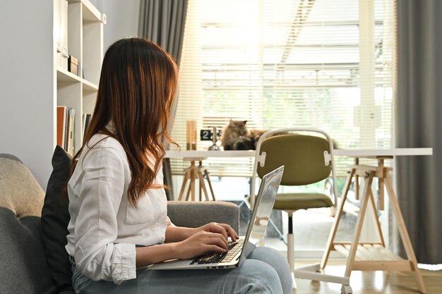 Vue latérale d'une jeune femme se reposant sur un canapé et vérifiant ses e-mails ou ses actualités en ligne sur un ordinateur portable Concept de technologie et de style de vie des personnes