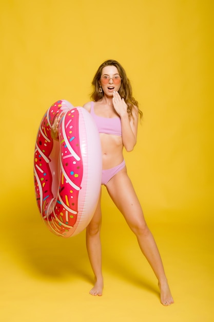 Vue latérale d'une jeune femme séduisante en maillot de bain lunettes de soleil à la mode tenant un anneau de bain en forme de beignet