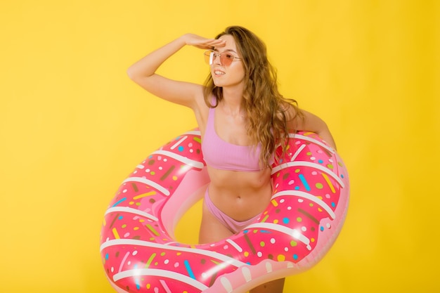 Vue latérale d'une jeune femme séduisante en maillot de bain lunettes de soleil à la mode tenant un anneau de bain en forme de beignet