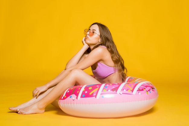 Vue latérale d'une jeune femme séduisante en maillot de bain lunettes de soleil à la mode tenant un anneau de bain en forme de beignet