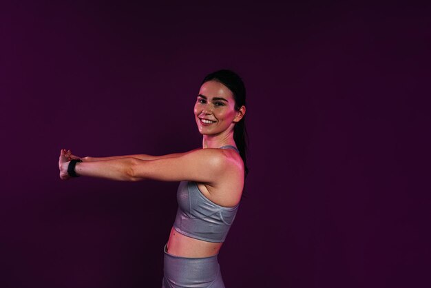 Vue latérale d'une jeune femme souriante s'étirant et fléchissant ses mains sur un fond magenta en studio