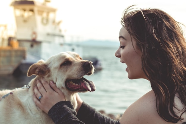 Vue latérale d'une jeune femme souriante tenant un chien sur la plage