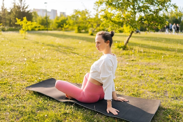 Vue latérale d'une jeune femme sportive faisant des exercices en pose de yoga assise sur un tapis se détendant dans un parc de la ville un jour d'été ensoleillé Concept de yoga en plein air forme physique mode de vie actif et sportif