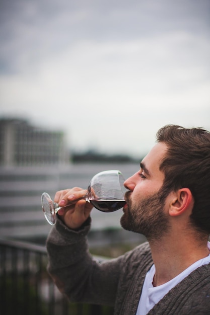 Vue latérale d'un jeune homme buvant du vin rouge contre le ciel