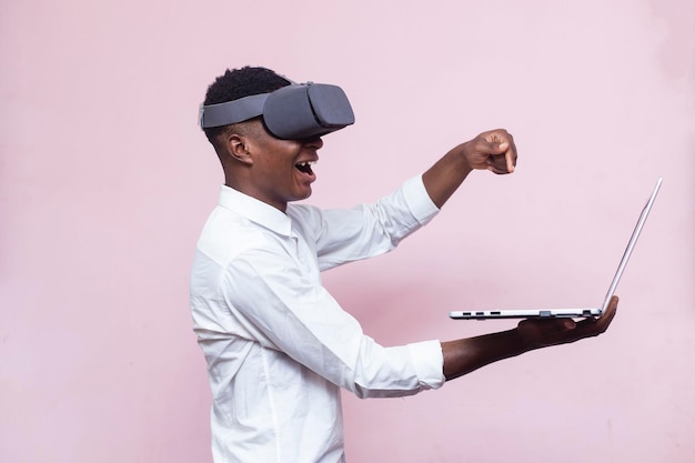 Vue latérale d'un jeune homme futuriste africain activant la réalité virtuelle avec un ordinateur portable à la main