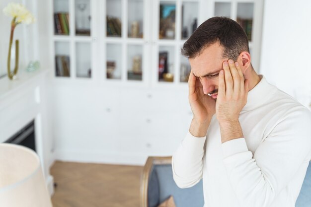 Vue latérale d'un jeune homme malheureux avec ses mains sur ses tempes regardant vers le bas