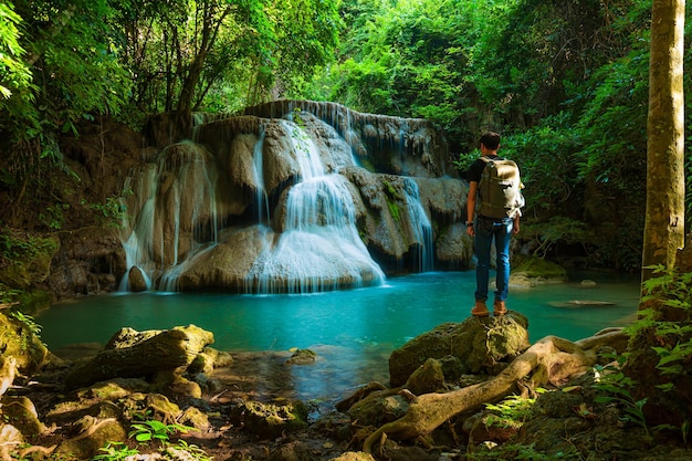 Vue latérale d'un jeune homme avec un sac à dos debout près d'une cascade en forêt