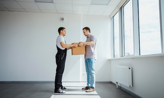 Vue latérale d'un jeune livreur heureux donnant une boîte en carton à un homme debout à l'intérieur