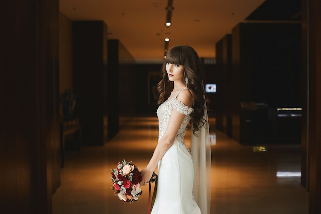 Vue latérale d'une jeune mariée en robe de mariée luxueuse à l'intérieur