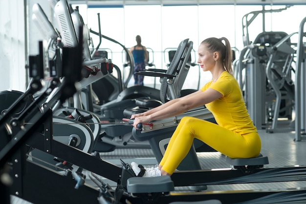 Vue latérale des jeunes femmes en forme à l'aide d'un rameur dans un club de santé