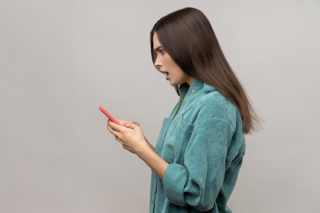 Vue latérale d'une jolie femme choquée lisant un message sur un smartphone avec la bouche ouverte à l'aide d'un appareil mobile