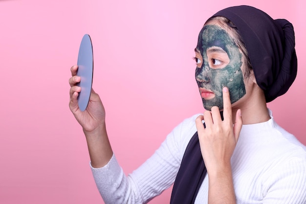 Vue latérale d'une jolie femme musulmane asiatique utilisant un masque et regardant dans le miroir Concept de beauté t