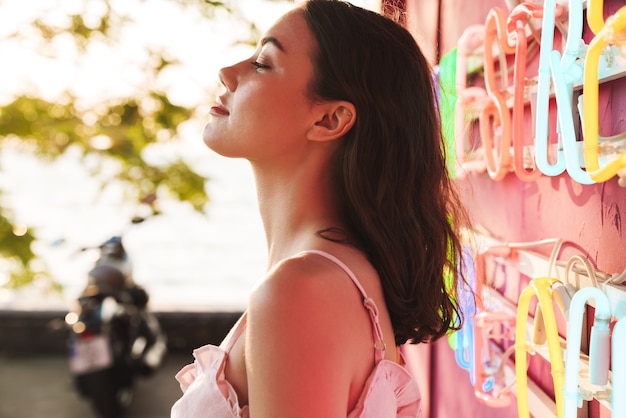 Vue latérale d'une jolie jeune femme détendue à la fête sur la plage près d'un mur coloré à led lumineux dans un café-bar.