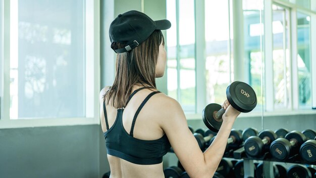 Vue latérale d'une jolie jeune femme sportive souriante avec haltère au club de gym fitness