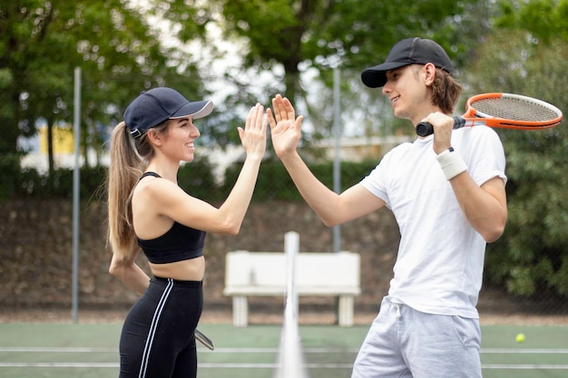 Vue latérale de joyeux joueurs de tennis masculins et féminins souriants qui se font la fête après avoir joué un bon match