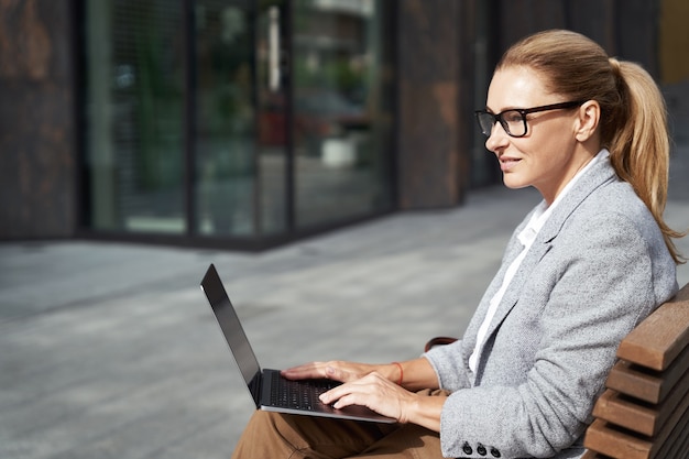 Vue latérale en ligne d'une femme d'affaires prospère travaillant sur un ordinateur portable tout en étant assise sur le