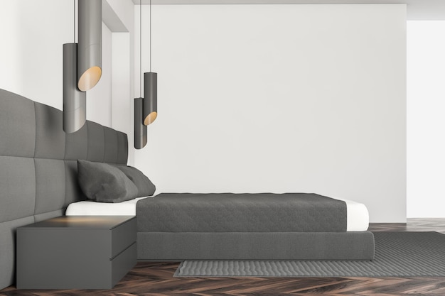 Vue latérale d'un lit gris dans un intérieur de chambre minimaliste avec des murs blancs, un sol en bois foncé et une table de chevet grise.