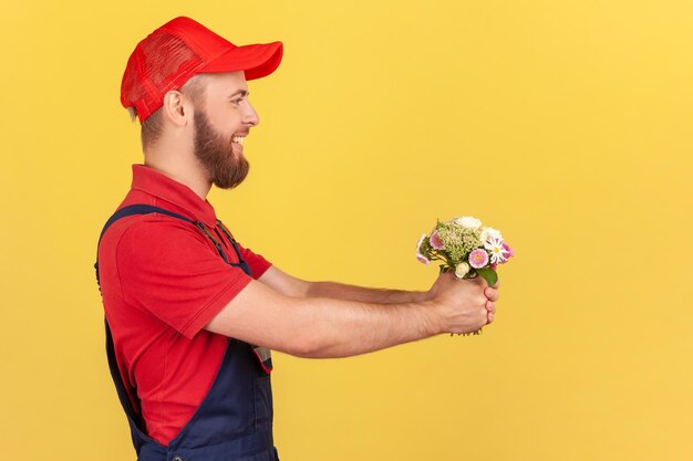 Vue latérale d'un livreur barbu satisfait et positif donnant un bouquet de fleurs mettant de l'ordre