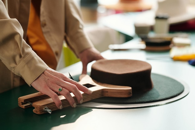 Vue latérale d'une main d'artisan utilisant un outil en bois pour façonner un chapeau