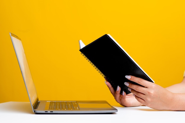 Vue latérale de la main et du livre lisant dans un bureau blanc Il y a un ordinateur portable à l'avant. concept de lecture de livre relaxant en lisant un fond jaune