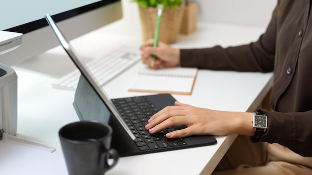 Vue latérale de la main féminine travaillant avec tablette numérique et écrit sur ordinateur portable sur table d'ordinateur