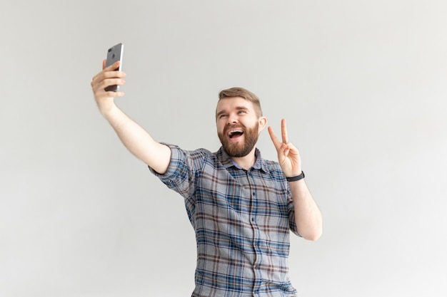 Vue latérale d'un mec drôle de hipster drôle positif et prenant un selfie sur un smartphone sur l'espace de copie de fond blanc. gadgets et technologies modernes.