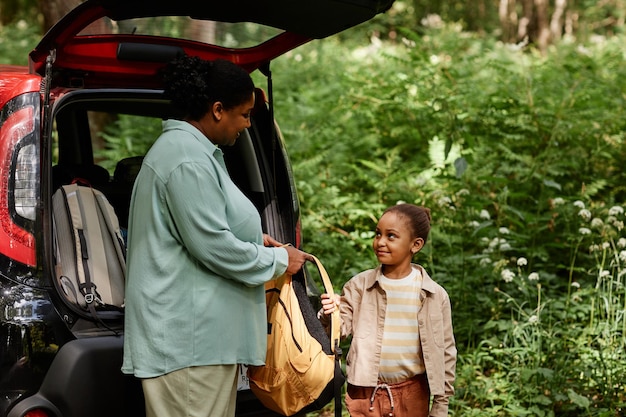 Vue latérale mère et fille afro-américaine debout en voiture sur le sentier