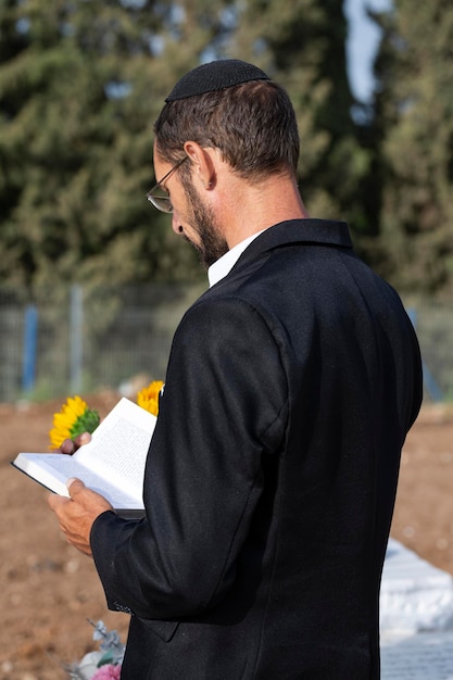 Vue latérale d'un mignon homme juif ultra-orthodoxe barbu priant dans la kippa et lisant une Bible hébraïque sur fond de forêt en Israël Mise au point sélective Juif hassidique lisant la Torah ou un livre par temps chaud