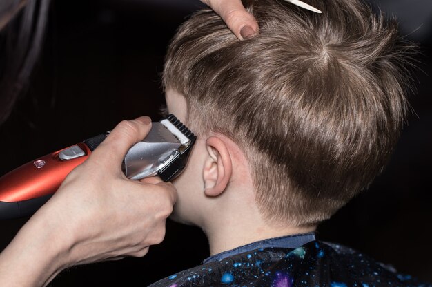 Vue latérale d'un mignon petit garçon se faisant couper les cheveux par un coiffeur au salon de coiffure.