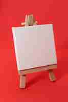 Photo vue latérale mini toile blanche avec chevalet en bois sur fond rouge