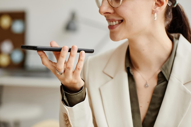 Vue latérale minimale d'une femme d'affaires souriante tenant un smartphone et enregistrant un message vocal