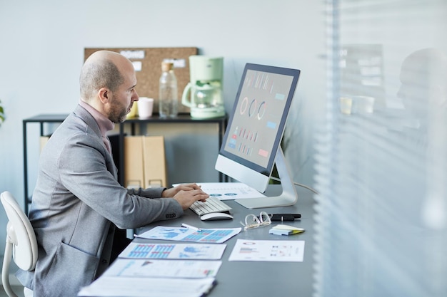 Vue latérale minimale d'un homme d'affaires mature utilisant un ordinateur lors de l'analyse de données dans le bureau de l'entreprise