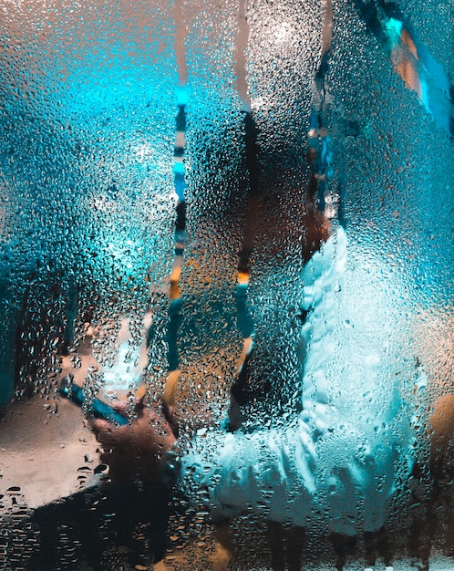Vue latérale d'une personne utilisant un téléphone vue à travers une fenêtre humide