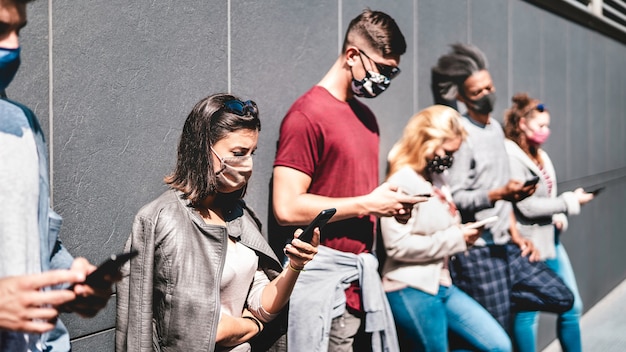 Vue latérale des personnes utilisant un téléphone mobile couvert par un masque facial - Focus sur la première femme à gauche