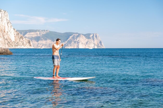 Vue latérale photo d'un homme nageant et se relaxant sur le sup board homme sportif dans la mer sur le stand