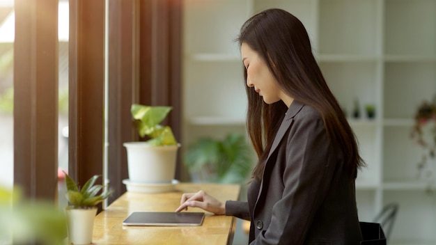 Vue latérale d'une pigiste en costume décontracté vérifiant son compte bancaire, travaillant sur sa tablette portable dans un café