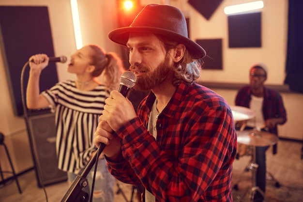 Photo vue latérale portrait de bel homme barbu chantant au microphone pendant la répétition