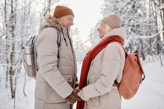 Vue latérale portrait d'un couple de personnes âgées heureux profitant d'une promenade dans la forêt d'hiver et se tenant la main