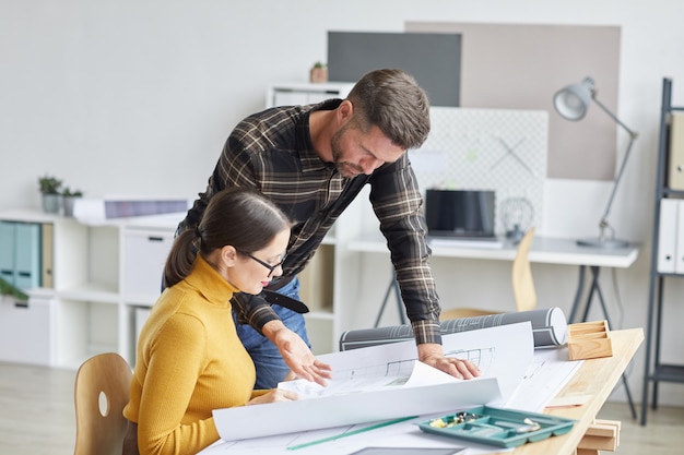 Vue latérale portrait de deux architectes collaborant sur des plans tout en travaillant ensemble au bureau,