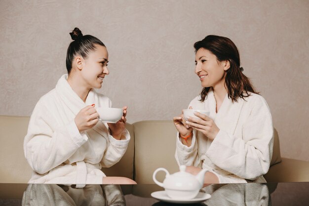 Vue latérale portrait de deux belle femme parlant avec une tasse de thé dans leurs mains après des procédures de spa habillé en peignoir dans un centre de bien-être.