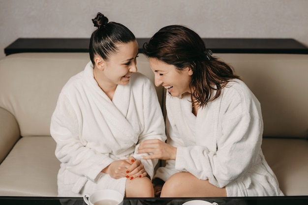 Vue latérale portrait de deux copines riant après un massage spa vêtus de peignoirs dans un centre de bien-être.